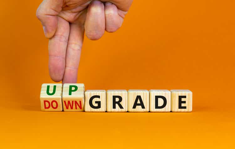 Upgrade or downgrade symbol. Businessman turns wooden cubes, changes words "downgrade" to "upgrade". Beautiful orange table, orange background, copy space. Business and upgrade or downgrade concept.