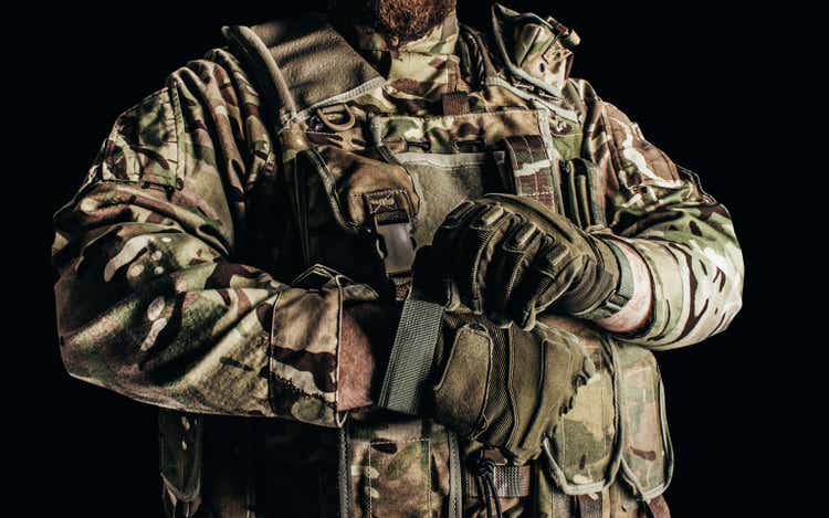 Soldier in level 3 camouflaged armored vest putting on tactical gloves.