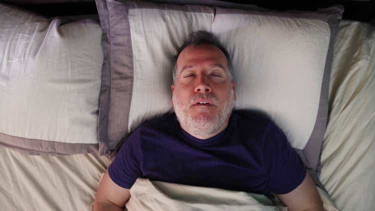 Mature man in bed sleeping on his back snoring with his mouth open