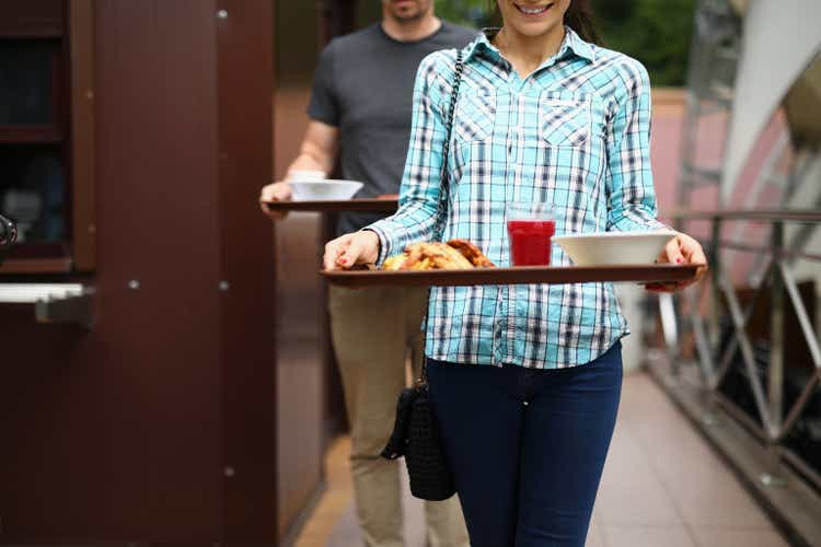 A woman and a man are carrying trays of food