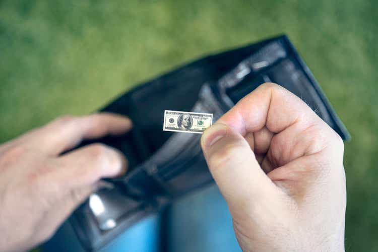 A male businessman opens a black wallet and pulls out a hundred-dollar bill on a green background. a small salary for an employee. concept of dollar inflation. Hand holding miniature dollar note