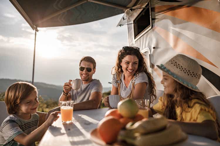 Happy family talking at picnic table by the camper trailer in nature.