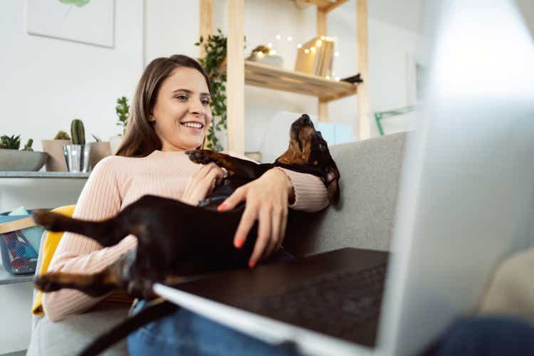 Smiling young woman holding her dog while working from home