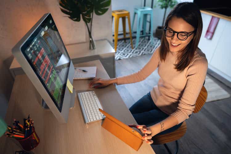 High-angle view of a young woman trading cryptocurrency on a computer and digital tablet