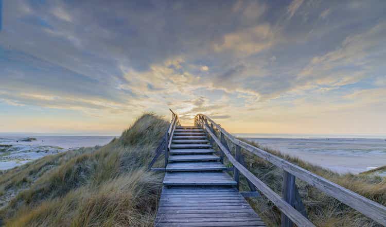 Boardwalk and stairs leading through the dunes to the beach of North Sea by sunset in Norddorf, Amrum, Schleswig-Holstein. Bathing and beach vacation on the North Sea.