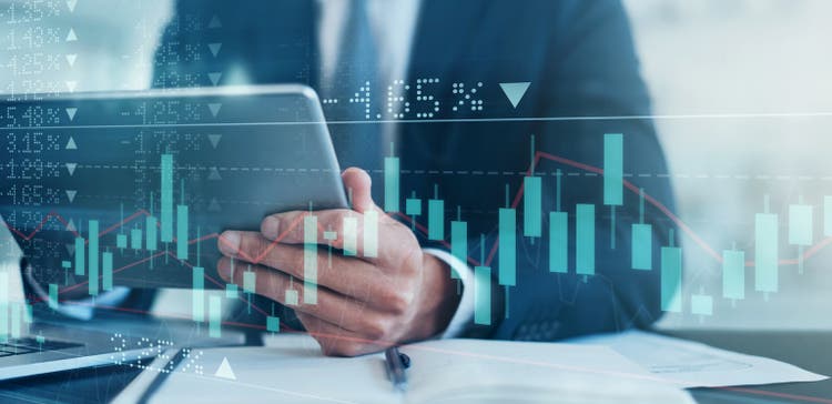لقطة محسّنة رقميًا لرجل أعمال لا يمكن التعرف عليه باستخدام جهاز لوحي تم تراكمه على رسم بياني يوضح الصعود والهبوط في سوق الأوراق المالية