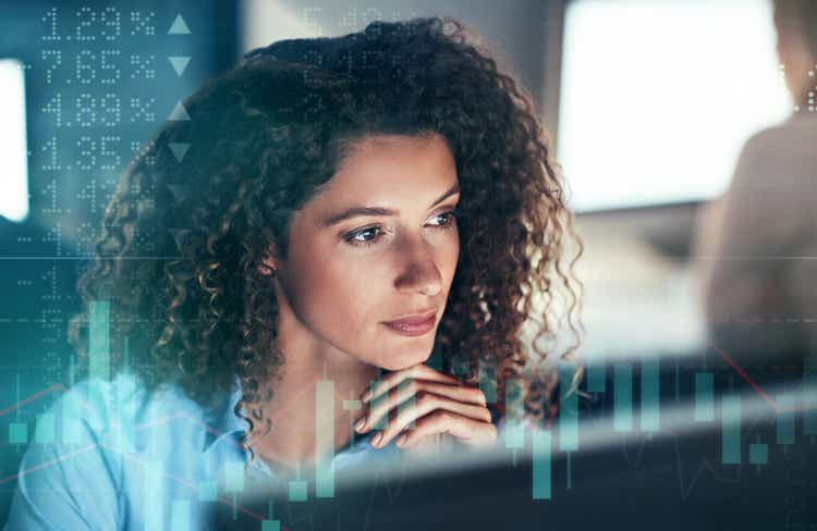 Digitally enhanced shot of an attractive businesswoman working in the office superimposed over a graph showing the ups and downs of the stock market