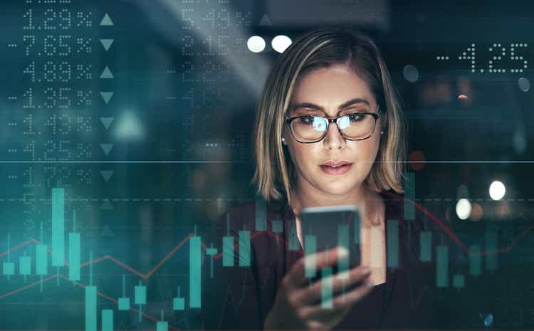 Digitally enhanced shot of an attractive businesswoman using a cellphone superimposed over a graph showing the ups and downs of the stock market