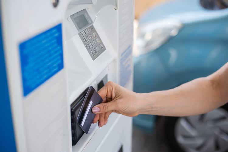 A woman fills her car with gasoline at a self-service gas station and pays with a credit card at a machine