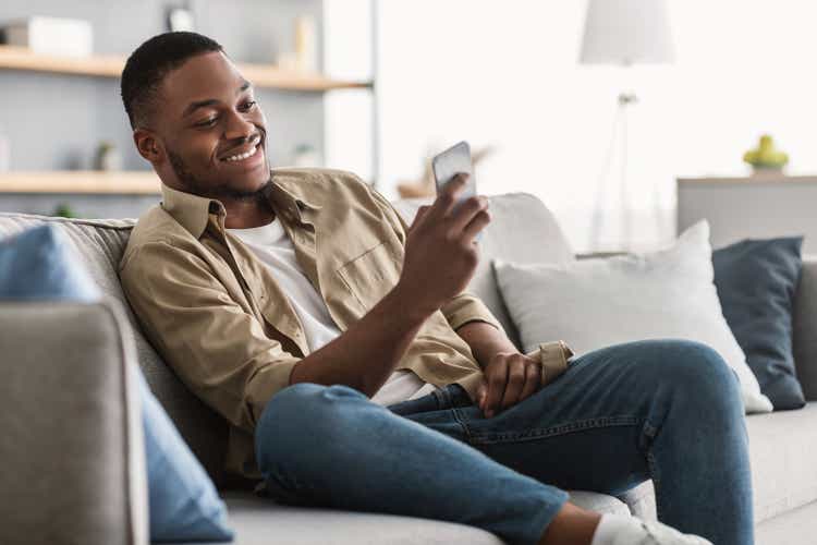 Side View Of African American Guy Using Smartphone At Home
