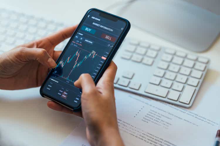 Close-up Shot of an Anonymous Woman Holding a Smartphone with a Stock Market Graph on Screen