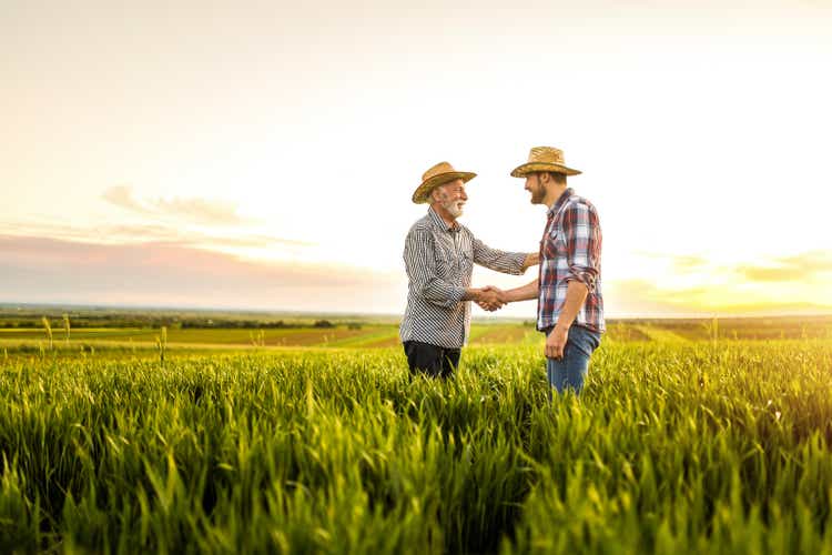 Two happy farmers shaking hands on an agricultural field.