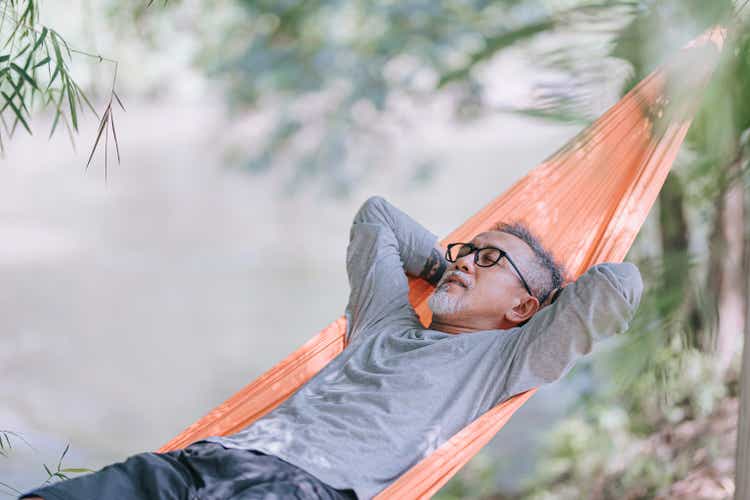 Asian Chinese senior man enjoying the afternoon lying in a riverside hammock under bamboo trees