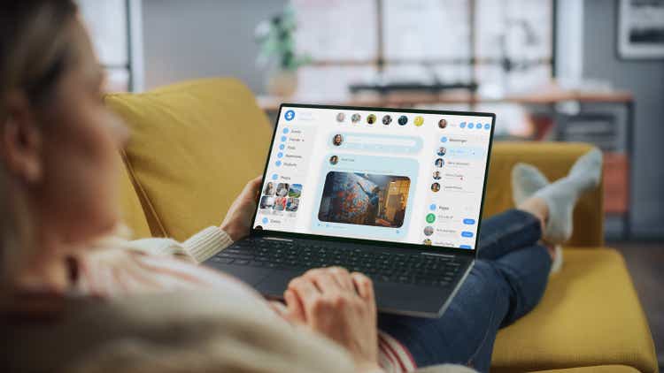 Beautiful Caucasian Female is Using Laptop for Chatting with Fiends in Social Network at Home Living Room while Lying on a Couch Sofa. Social Media Marketer Working From Home, Surfing the Internet.