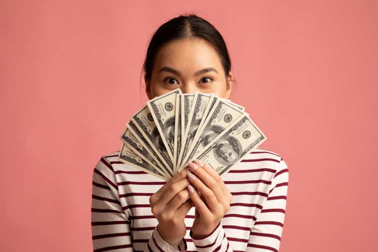 Big Profit. Happy Young Asian Woman Covering Face With Dollar Cash Fan