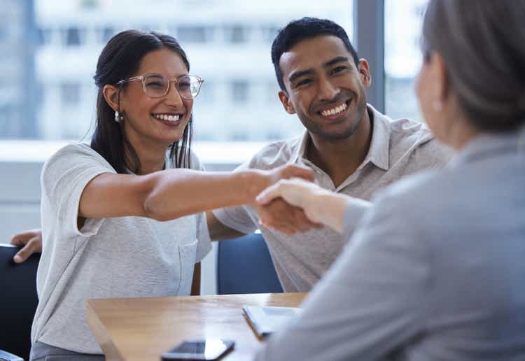 Shot of a young couple sharing a handshake with a consultant they"re meeting to discuss paperwork an office