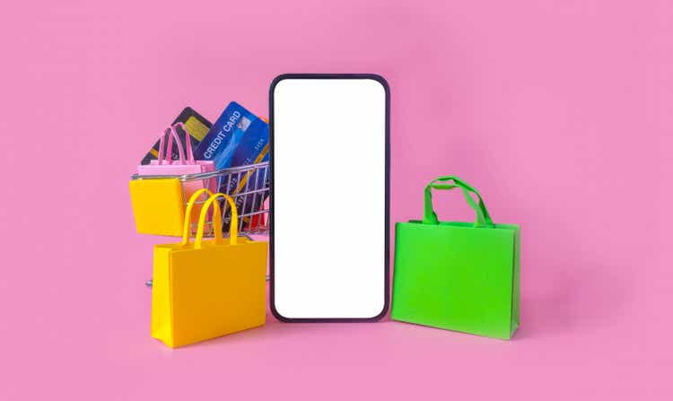 Shopping and payment with smartphone white screen and shopping bag, credit card in cart on pink background.Consumers can buy everything from online stores using a smart device connects to internet.