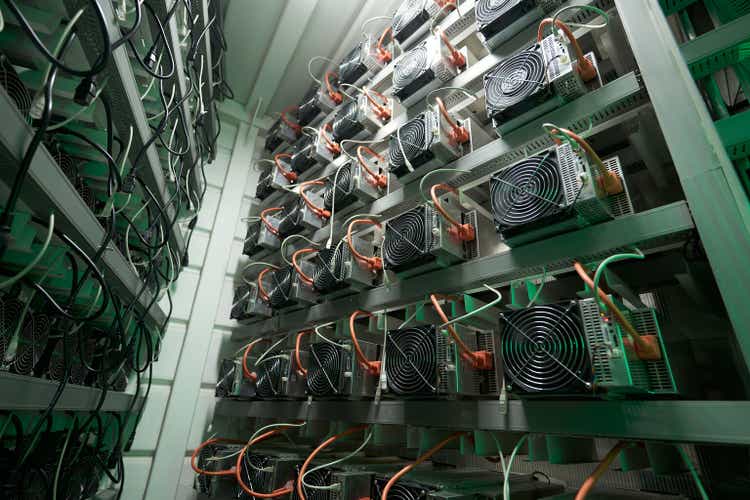 Bitcoin miners in large farm. ASIC mining equipment on stand racks mine cryptocurrency in steel container. Blockchain techology application specific integrated circuit datacenter. Server room lights