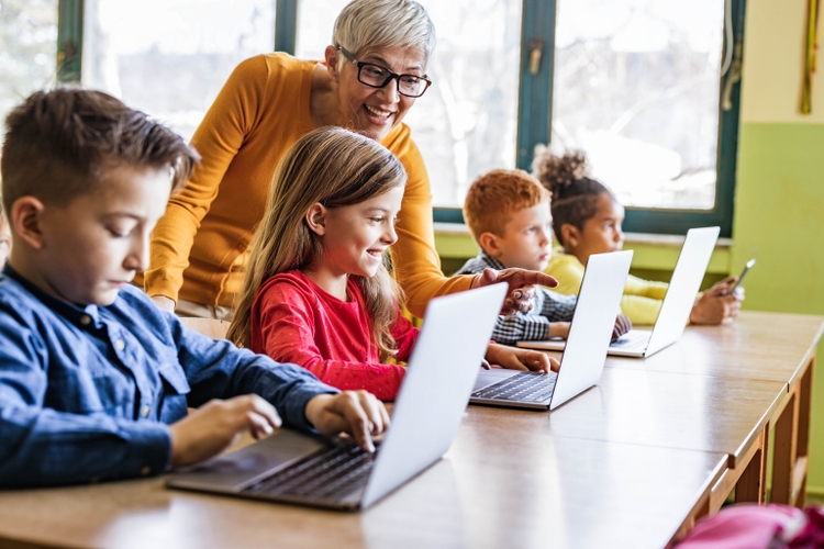 Happy mature teacher assisting her students on computer class at school.