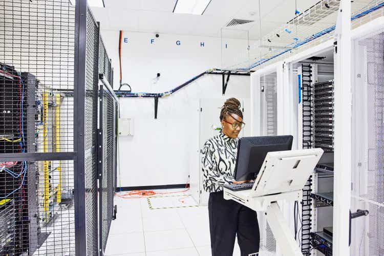 Medium wide shot of female computer engineer configuring server in data center