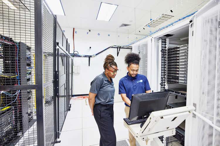 Medium wide shot of IT professionals in discussion while configuring server in data center