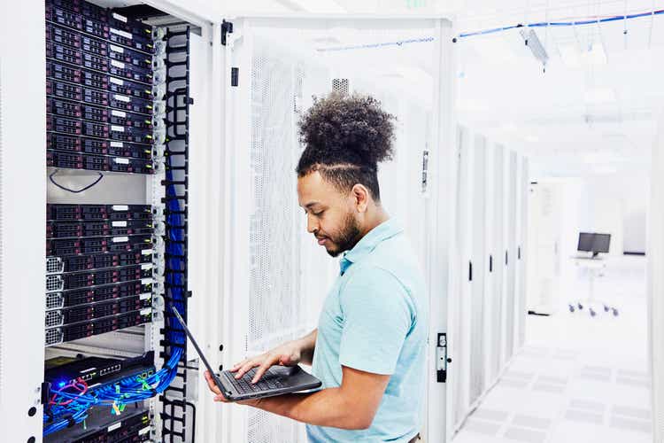 Medium shot of male IT professional looking at laptop while working on server in data center