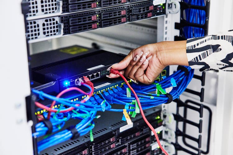 Close up shot of female IT professionals hand connecting ethernet cable to router in server rack while working in data center