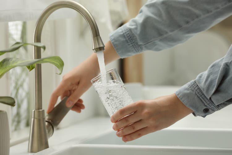 Woman filling glass with water from tap at home, close-up