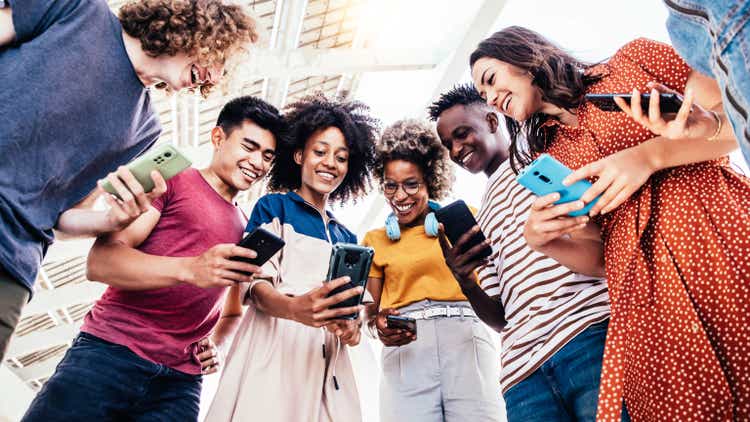 Diverse teenage students using digital smart phones mobile at college campus - Group of friends watching cellphones sharing content on social media platform - Youth, friendship and technology concept