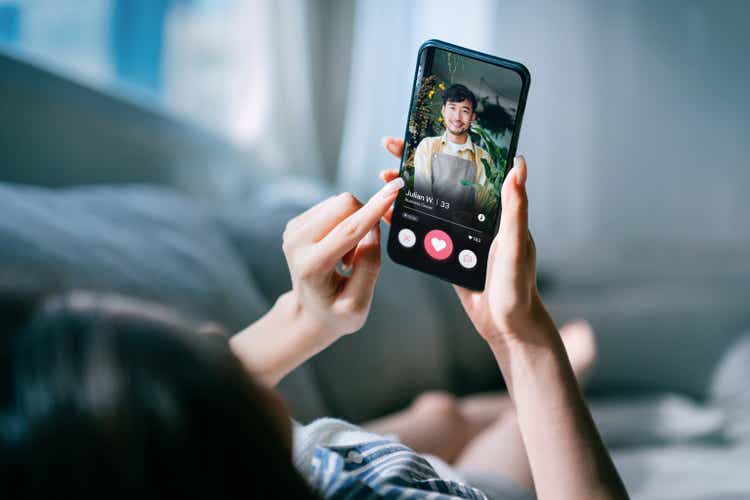 Young Asian woman lying on sofa at home, using an online dating app on smartphone, looking for love on the internet. Social media. Internet dating. Couple relationship. Love concept