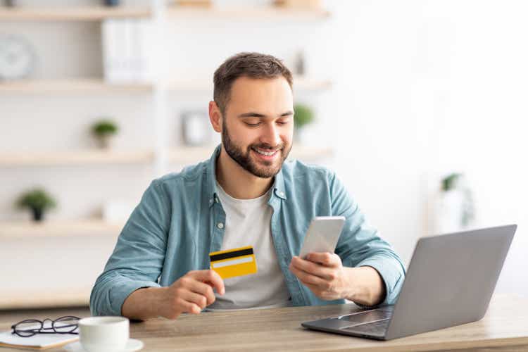 Šťastný kavkazský muž nakupuje věci online, používá smartphone, notebook a kreditní kartu, užívá si nakupování na internetu