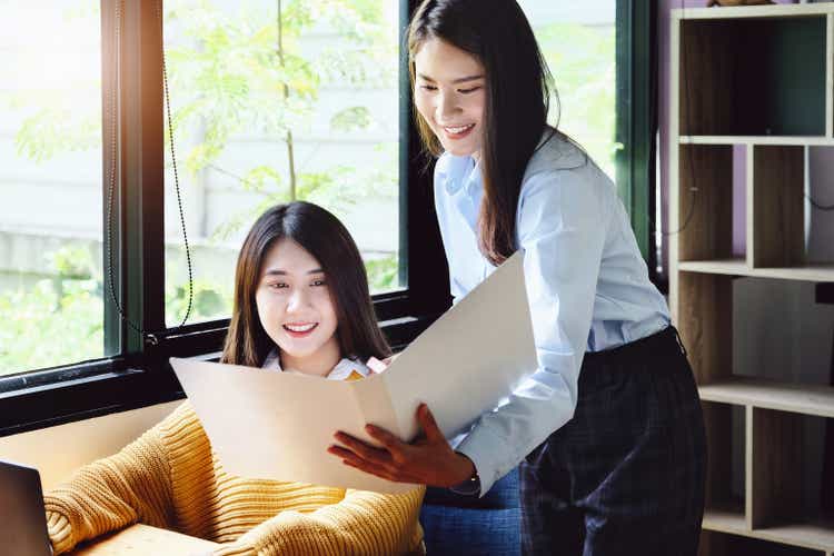 Two female company employees happily smiled at each other as they handed each other folders.