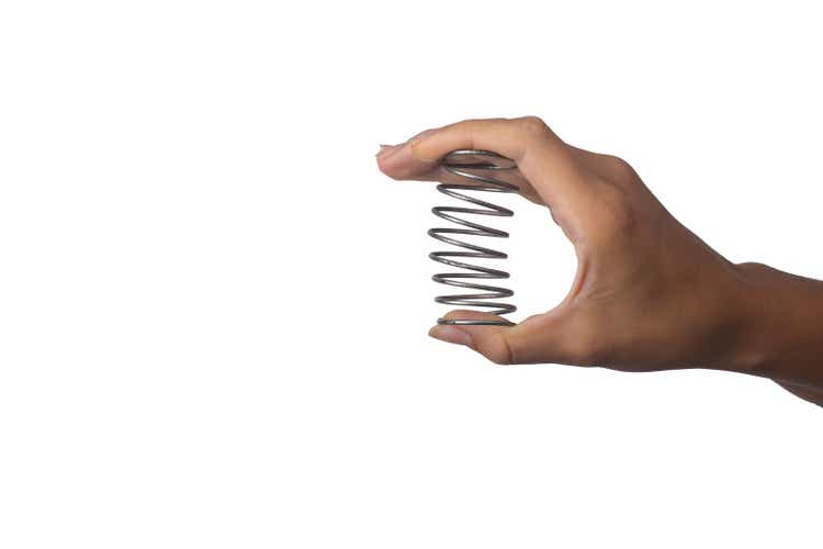 A female hand squeezes a metal spring on a white background.