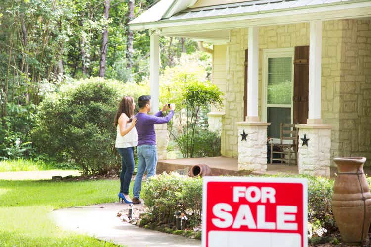 Mid adult couple are considering purchasing a new home. For sale sign in foreground.