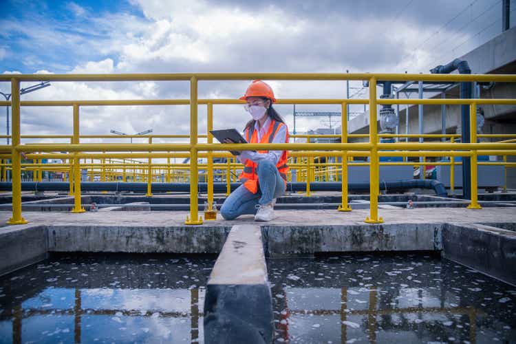 Worker take water from the wastewater treatment pond to check the quality of the water. After going through the wastewater treatment process,she wearing face mask to protect pollution in work.