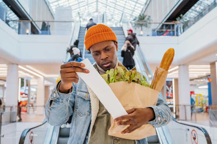 Surprised black man looks at receipt total with food at shopping mall