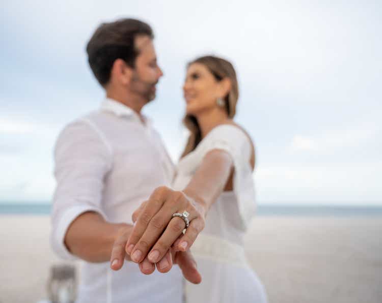 Couple getting engaged at the beach and showing the ring to the camera