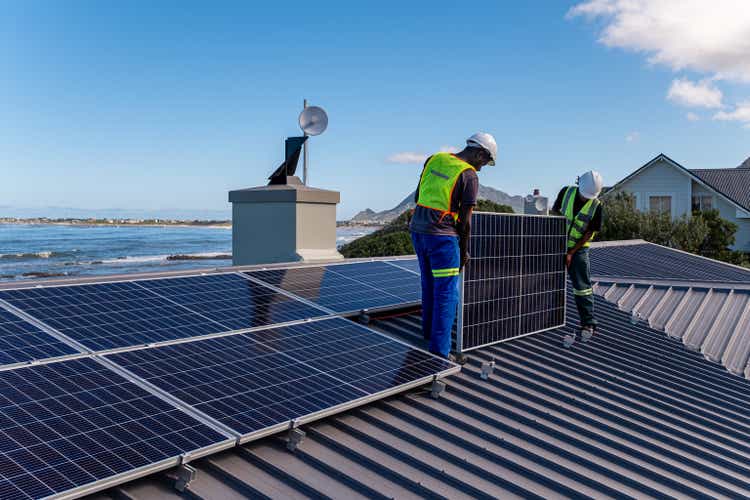 Two technicians install solar panels on a residential building