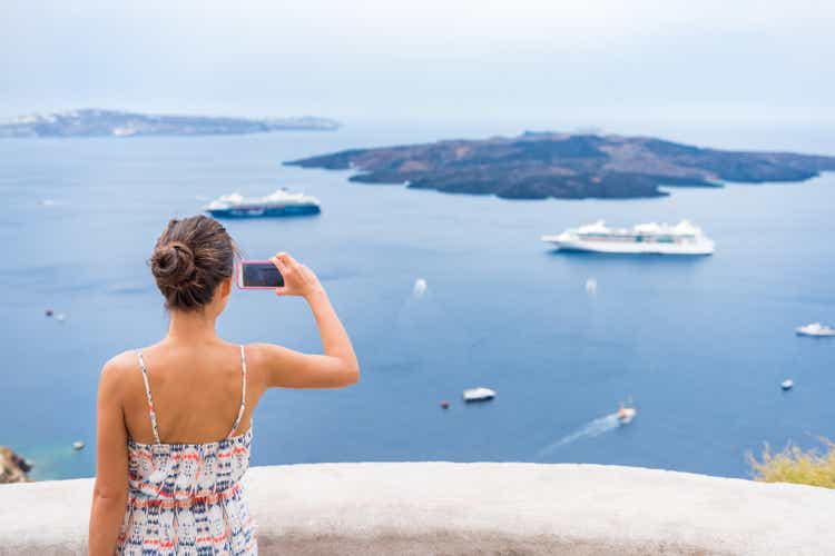 Europe cruise vacation summer travel tourist woman taking picture with phone of Mediterranean Sea in Santorini, Oia, Greece, with cruise ships sailing in ocean background