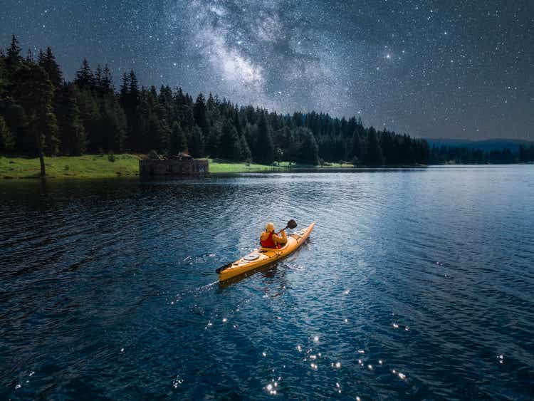 Woman kayaking in mountain lake under Milky way. Aerial view with starry sky. Paddling and ecotourism.