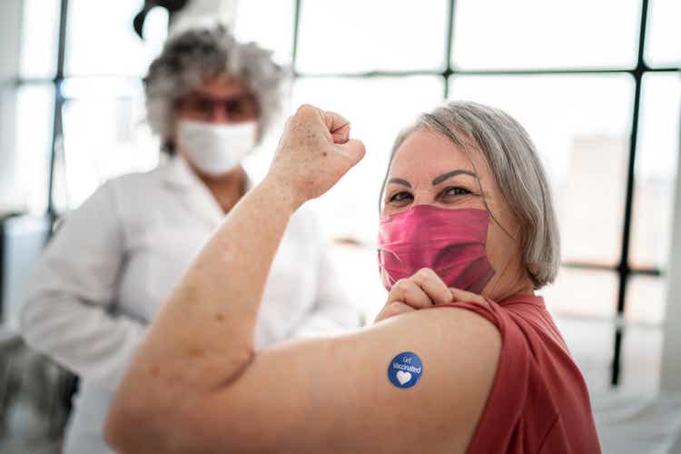 Vaccinated senior woman flexing biceps muscle with "Got vaccinated" sticker on - wearing face mask