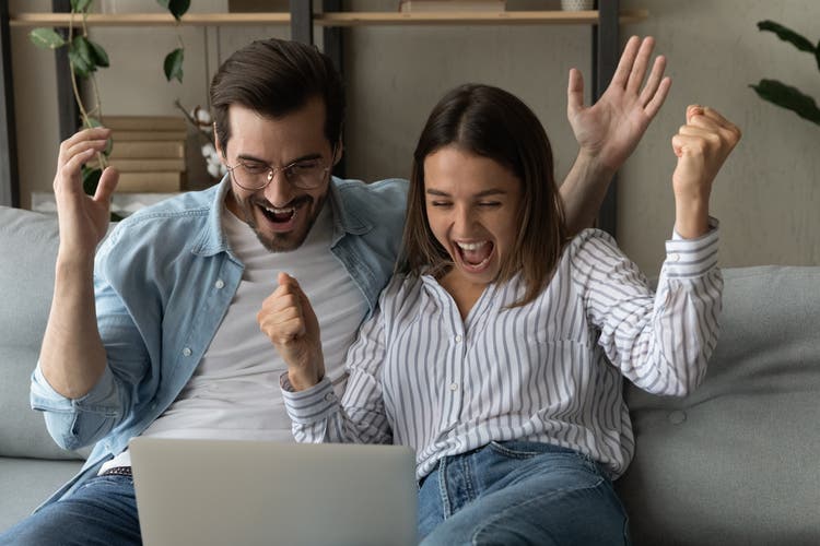 Euphoric couple read unbelievable news on laptop celebrate success