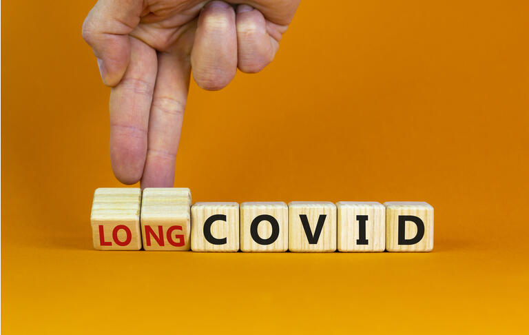 Long covid symbol. Doctor turnes wooden cubes and changes words "covid" to "long covid". Beautiful orange background, copy space. Medical, covid-19 pandemic long covid concept.