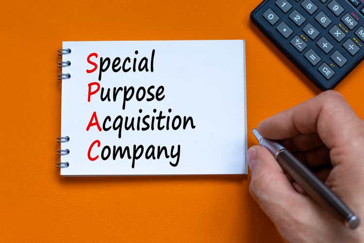 SPAC, special purpose acquisition company symbol. Words "SPAC, special purpose acquisition company on white note on orange background, copy space. Black calculator. Business and SPAC vs IPO concept.