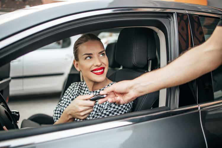New car owner sitting in car and taking keys from seller