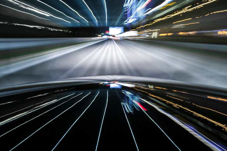 Black German car drives out of the city while night on illuminated street.