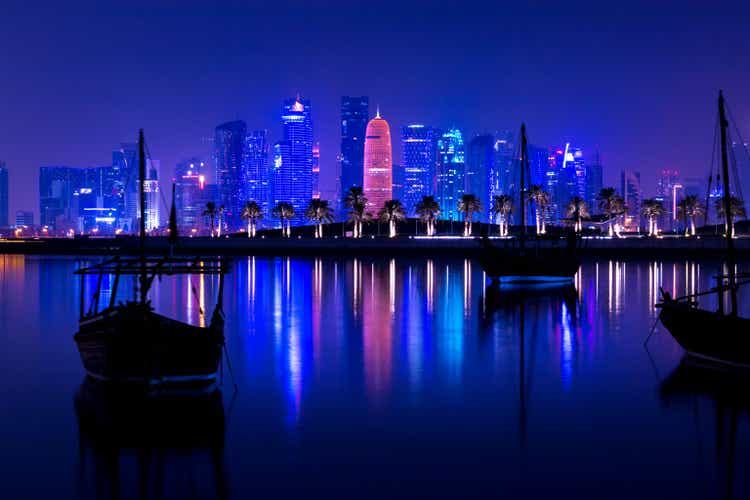 Coloful illuminated skyline of Doha at night with traditional wooden boats called Dhows in the foreground, Qatar