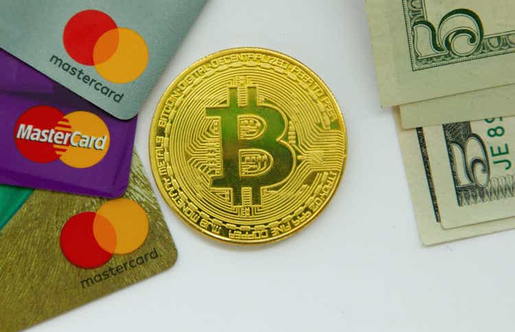 Bitcoin coin between three mastercard cards and dollar bills on white background
