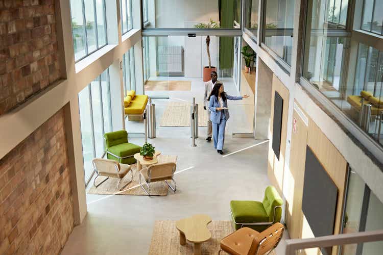 Real Estate Agent Leading Client Through Modern Office Building Lobby