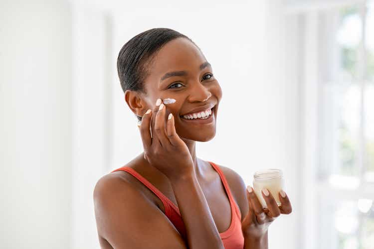 Happy black mature woman applying cream on face